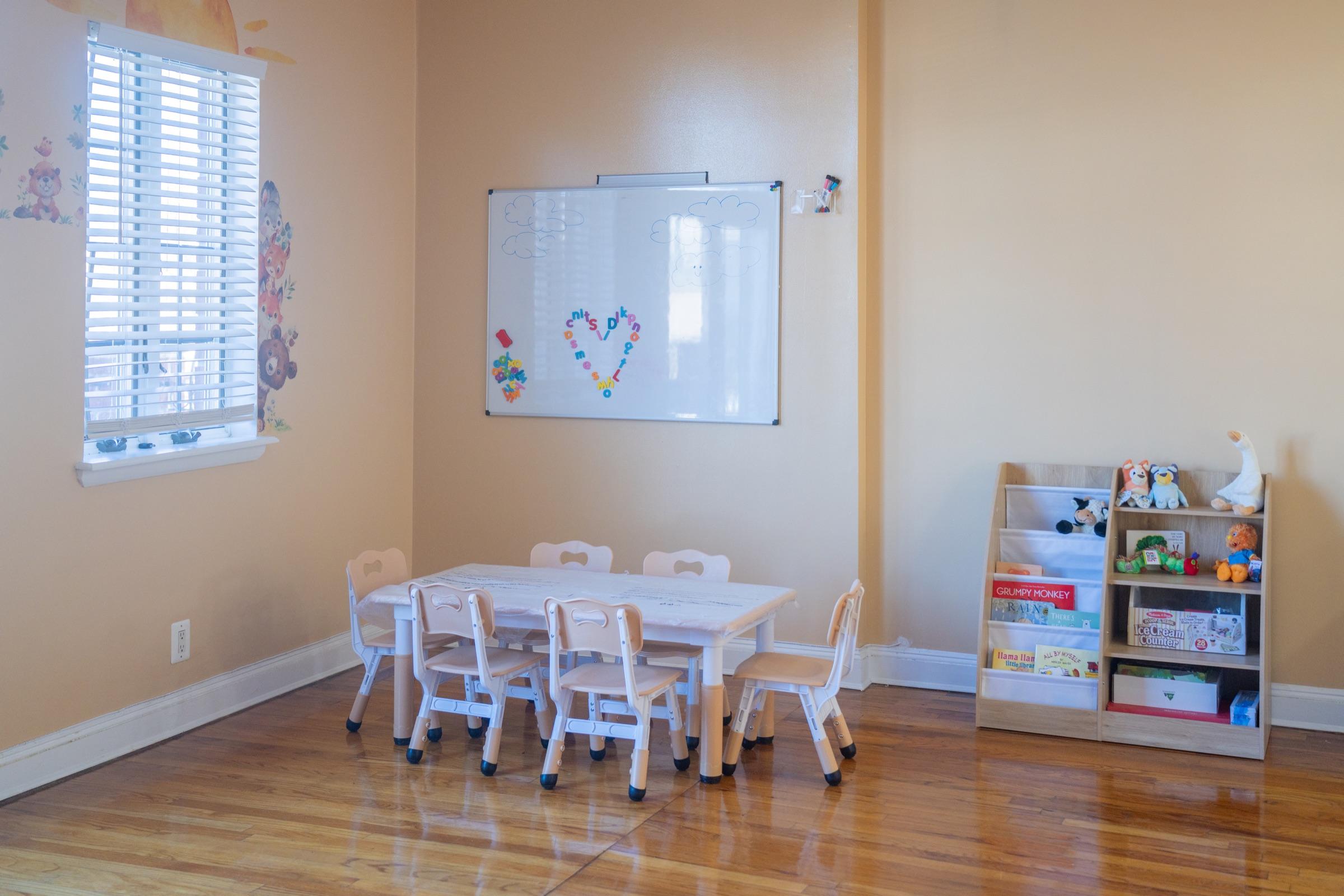 Bright learning room with child-sized tables, books, and a whiteboard.